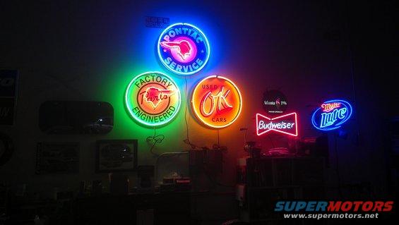 Collection of neon signs including Pontiac Service, Factory Engineered, Used OK Cars, Budweiser, and Miller Lite