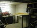 2004 Aston Martin Virage - A workshop area with a wooden workbench, tool chest, and shelves filled with various items.