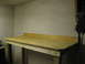 2004 Aston Martin Virage - A simple wooden workbench is set against a pegboard wall in a dimly lit room.