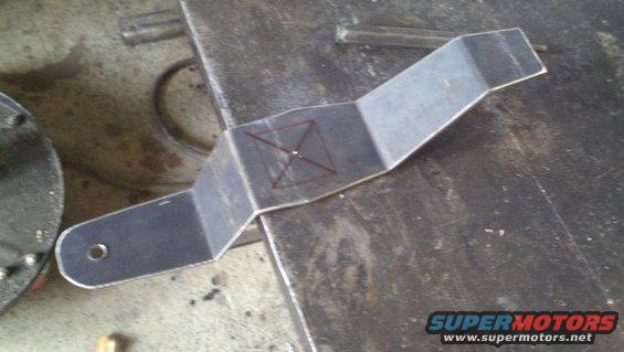 Custom metal bracket with scribe marks for drilling, resting on a workbench