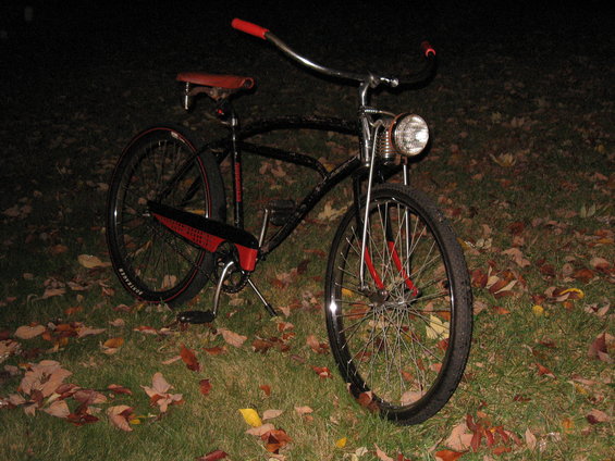 Black bicycle with red handlebars and seat, chrome headlight, and red accents on the frame and fenders