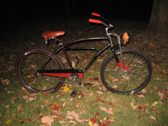 Black vintage bicycle with red handlebars and seat, parked on grass with fallen leaves