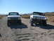 1988 Ford Bronco - Two white Ford trucks, likely from the early 1990s, are seen off-roading on a dirt path.
