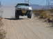 1988 Ford Bronco - A white off-road truck takes flight over a dirt hill, kicking up dust in a desert landscape.