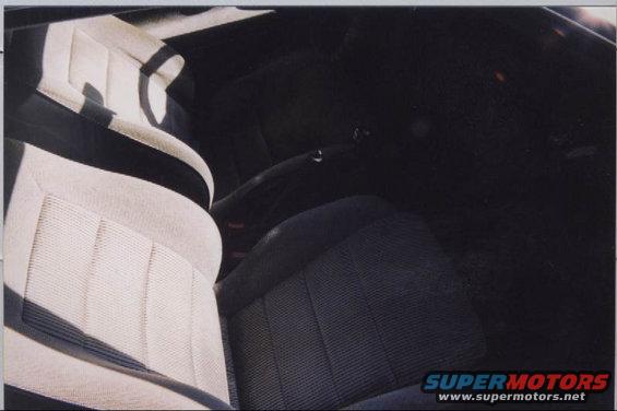 Car interior with light-colored front seats and dark rear seats. Center console and dashboard are visible in the dark