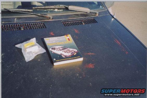 Car hood with a Haynes repair manual for a 1975-1984 Volkswagen Scirocco and a plastic bag containing car parts