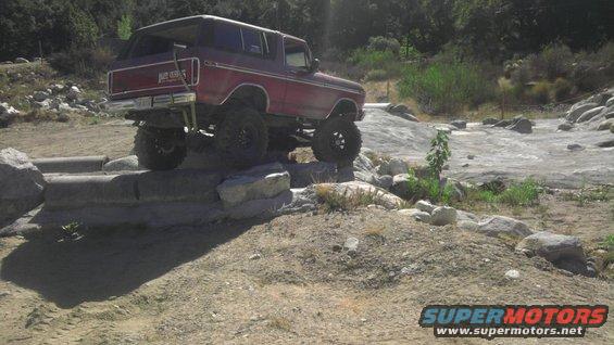 Red 1978 Ford Bronco with lifted suspension driving over rocks