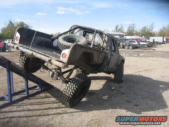 Muddy pickup truck with roll cage and spare tire in bed, on a ramp