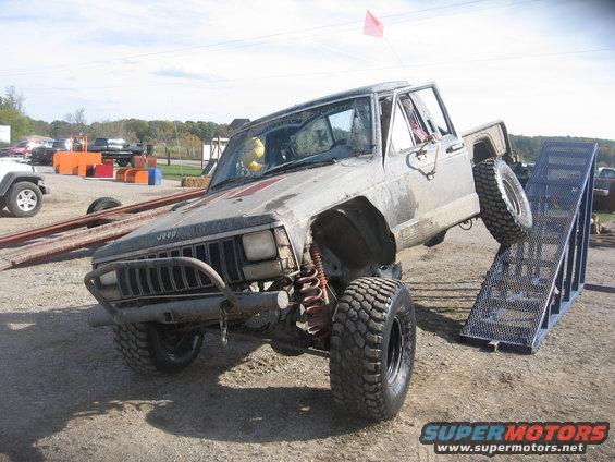 1987 Jeep Comanche pickup truck with lifted suspension, off-road tires, and a brush guard, climbing a metal ramp