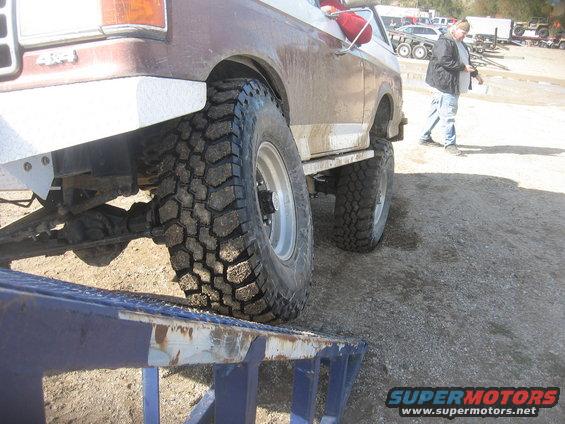 Brown pickup truck with large tires on a ramp, showing its rear fender and suspension