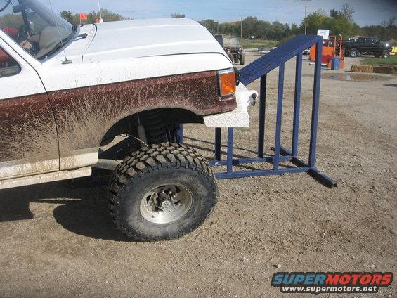 Mud-covered pickup truck with large tires next to a metal ramp