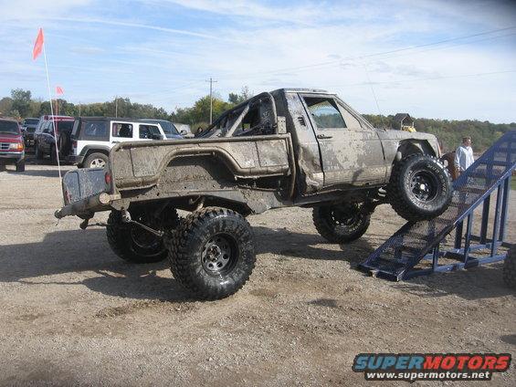 Mud-covered Jeep pickup truck on a ramp, with other vehicles in the background
