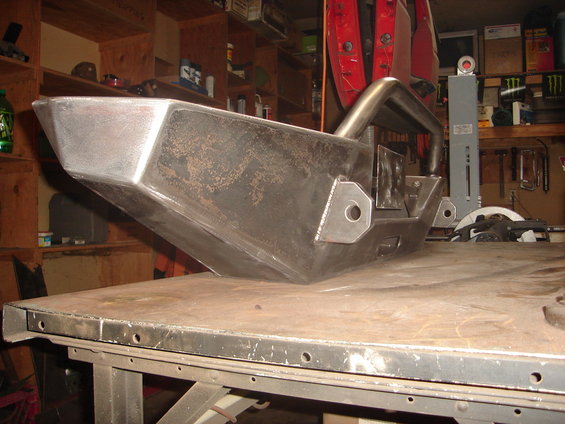 Unfinished metal bumper with integrated roll bar, resting on a workbench