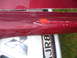 1993 Mazda MX-3 - Close-up of a damaged red car side skirt, revealing a Mitsubishi emblem and part of a license plate.