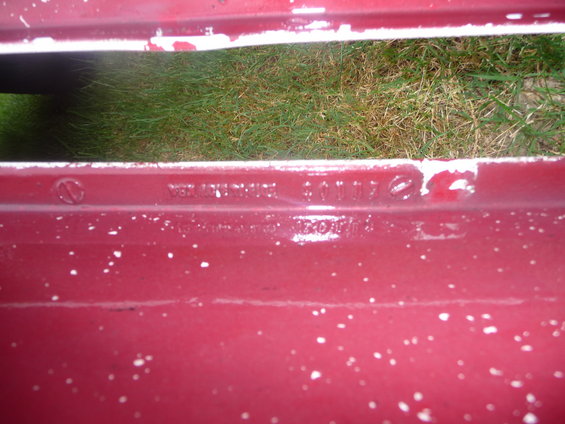 Red car part with white speckles and stamped text 'VER. MAZDA-THOMSON 601107 NECOAT' and other illegible markings