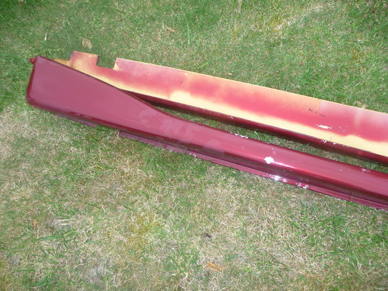 Maroon car side skirts with yellow primer underneath, lying on grass