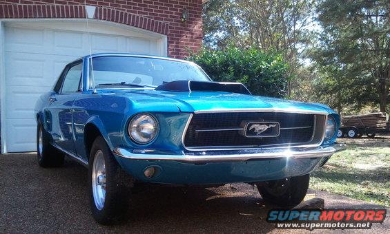 Blue 1967 Ford Mustang with a hood scoop parked in front of a garage