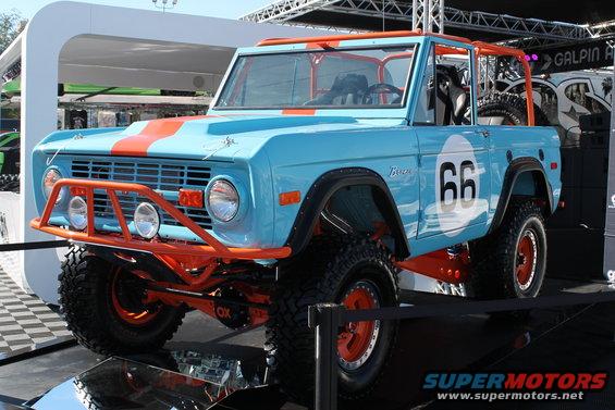 Light blue Ford Bronco with orange stripes and '66' graphic, lifted with off-road tires