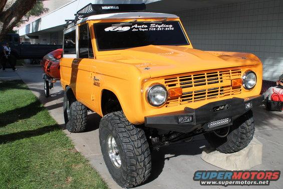 Orange Ford Bronco with Yakima rack and custom bumper. Has 'Bronco' badge on fender and 'RAD Auto Styling' sticker on windshield