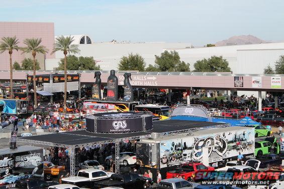Outdoor car show with palm trees, display booths, and numerous cars