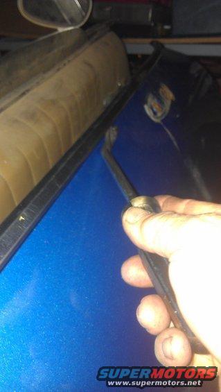Hand using a trim tool on the edge of a blue car door near tan interior upholstery