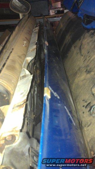 Blue car door with chipped paint and rust on the edge, seen from the side