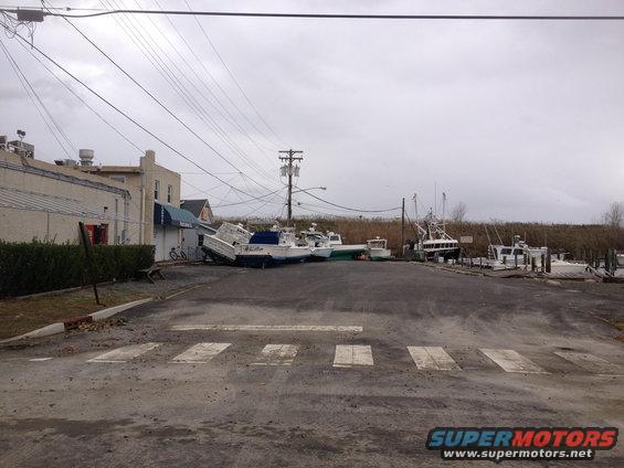 Boats are scattered on land near buildings and power lines, some tilted on their sides