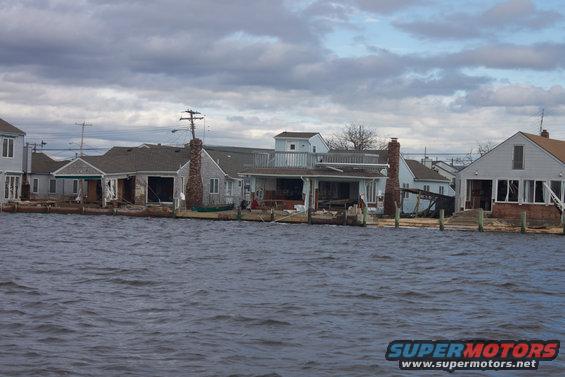 Flooded houses with damaged structures and debris, viewed from the water