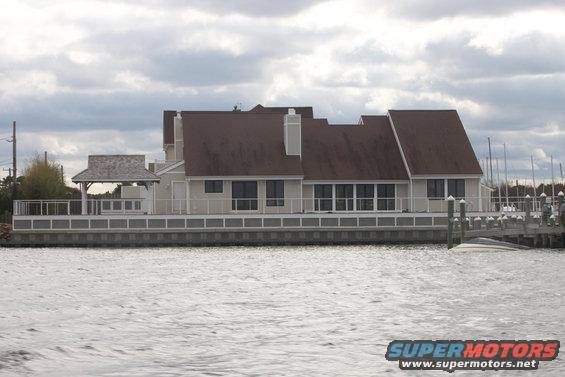 Partially submerged boat next to a wooden dock with a large house in the background