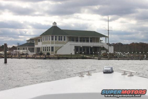 White boat bow with cleat and antenna, overlooking a marina and building