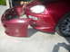 1993 Mazda MX-3 - A detached red front bumper cover rests beside a 1993 Mazda MX-3, revealing its headlights and fender.