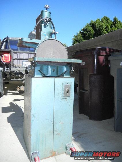 Blue disc sander with red casters, parked next to a truck and trash bins