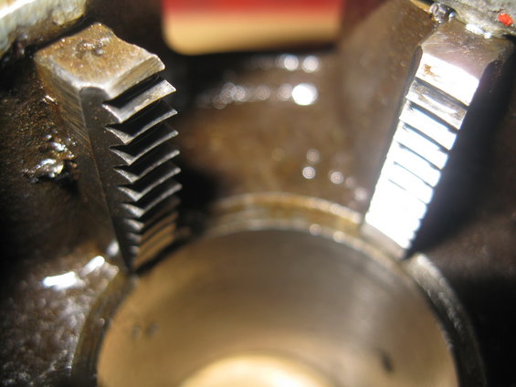Close-up of two metal gears with teeth, one on the left with a V-shaped cut pattern, the other on the right with straight cuts, in a dark, oily environment