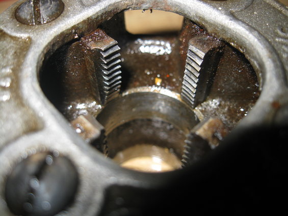 Close-up of a metal pipe threading die with visible teeth and oil