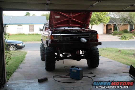 Red Ford truck with hood open, lifted suspension, and large tires, parked in a garage