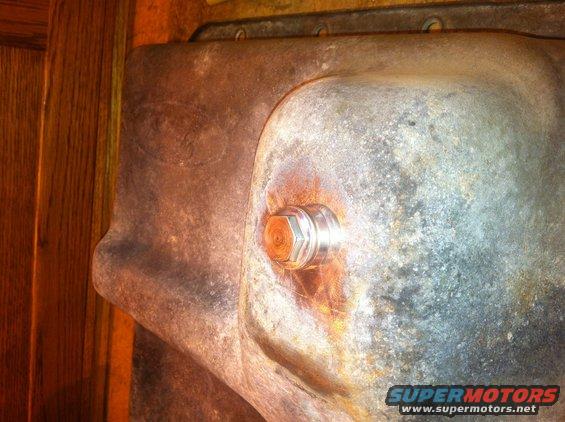 Close-up of a transmission oil pan drain plug on a rusty metal surface