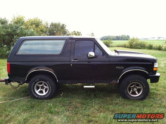 Side view of a black 1992 Ford Bronco with aftermarket wheels and some rust on the rear fender