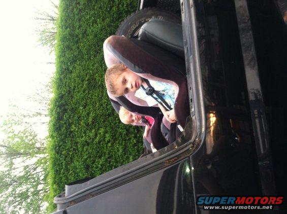 Children in car seats inside a black vehicle