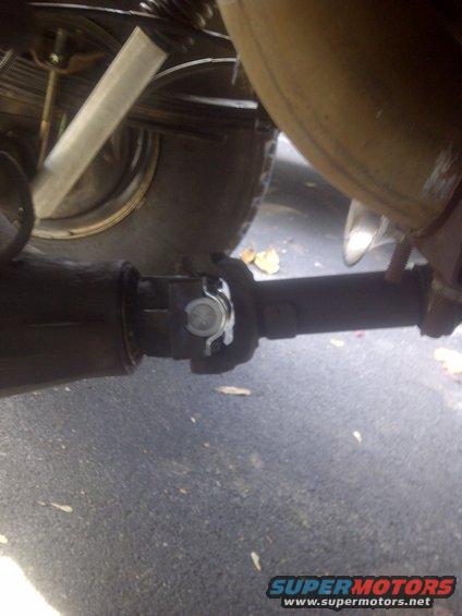 Close-up of a vehicle's driveshaft connecting to the rear axle, with a tire and suspension visible