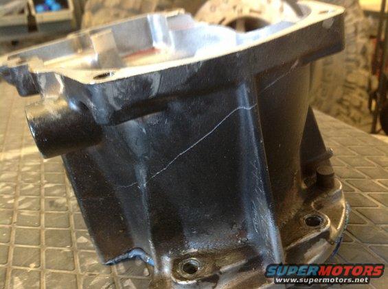 Cracked black metal automotive part with visible white lines indicating fractures