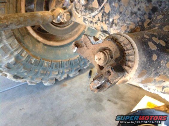 Close-up of a broken U-joint on a muddy vehicle axle near a tire