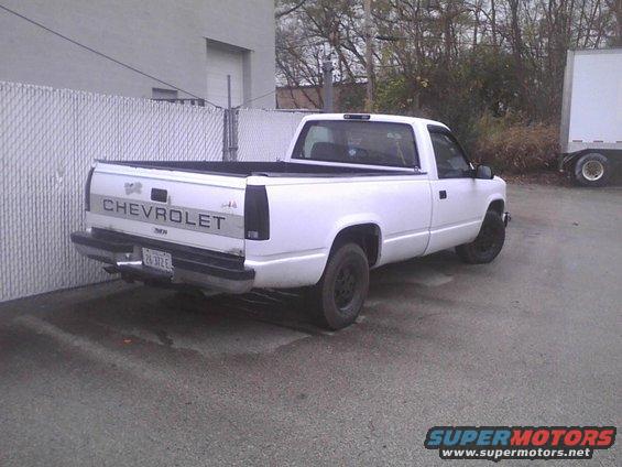 White Chevrolet pickup truck parked next to a fence and a box truck