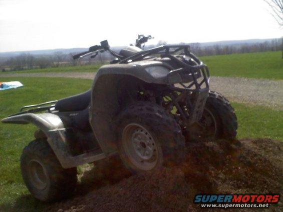 Olive green four-wheeler on dirt mound, front right wheel elevated
