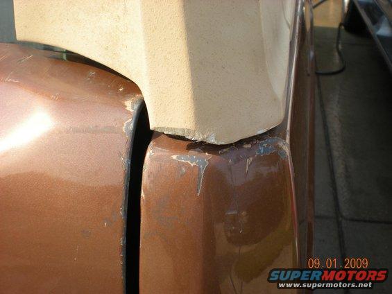 Close-up of the seam between two brown painted vehicle body panels, with a tan trim piece above