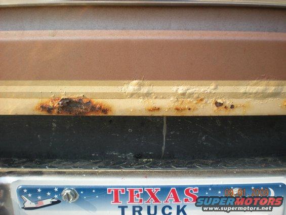 Close-up of rust on a brown and tan vehicle panel above a Texas license plate