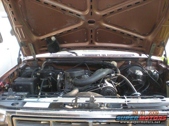 Brown 1980s truck engine bay with hood open, showing V8 engine, hoses, and wiring
