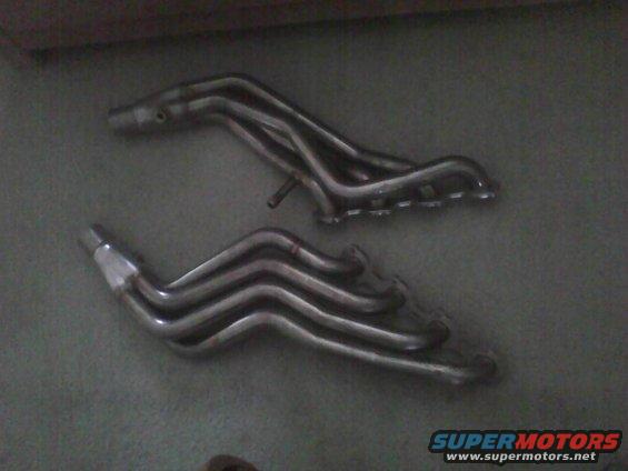 Two chrome exhaust headers on a dark surface, one above the other