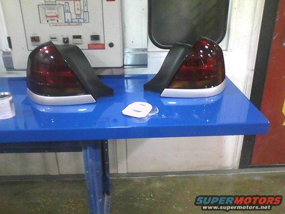 Two car tail lights on a blue table, with a diagram on the wall behind