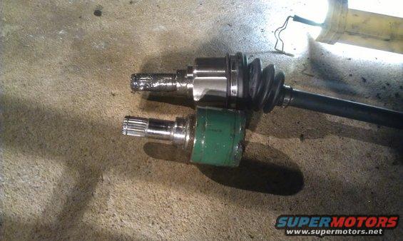 Two CV axles on a concrete surface. One axle has a green boot, the other has a black rubber boot