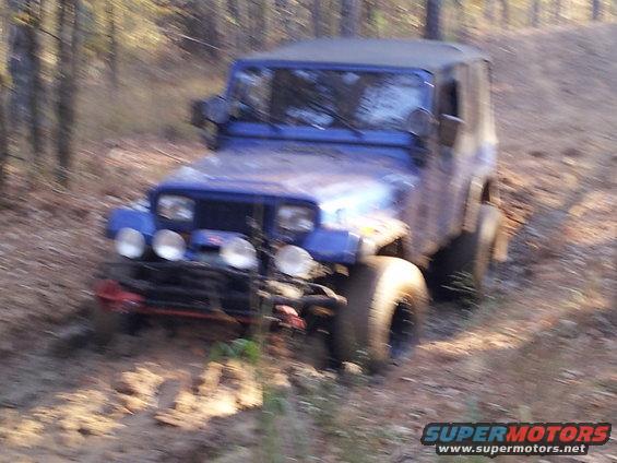 Blue Jeep Wrangler with off-road tires and winch on a dirt path